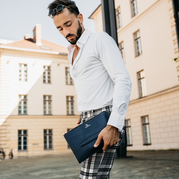 Man holding blue leather crossbody hand bag with gold zipper and logo