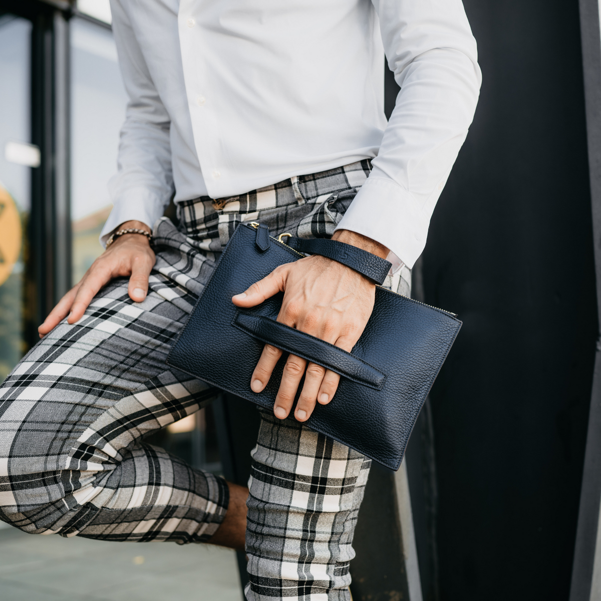 Man carrying blue leather men’s hand bag with top handle and gold zipper detail