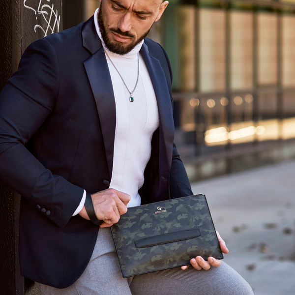 Green camouflage leather hand bag on lap, showing front pocket and gold-tone zipper