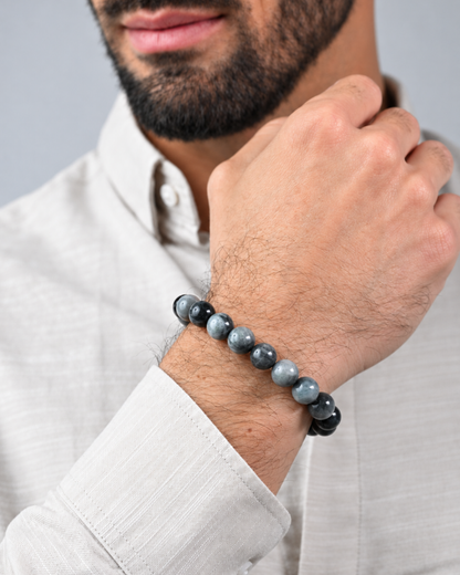 Gray beaded bracelet on wrist with black cord and metal tag