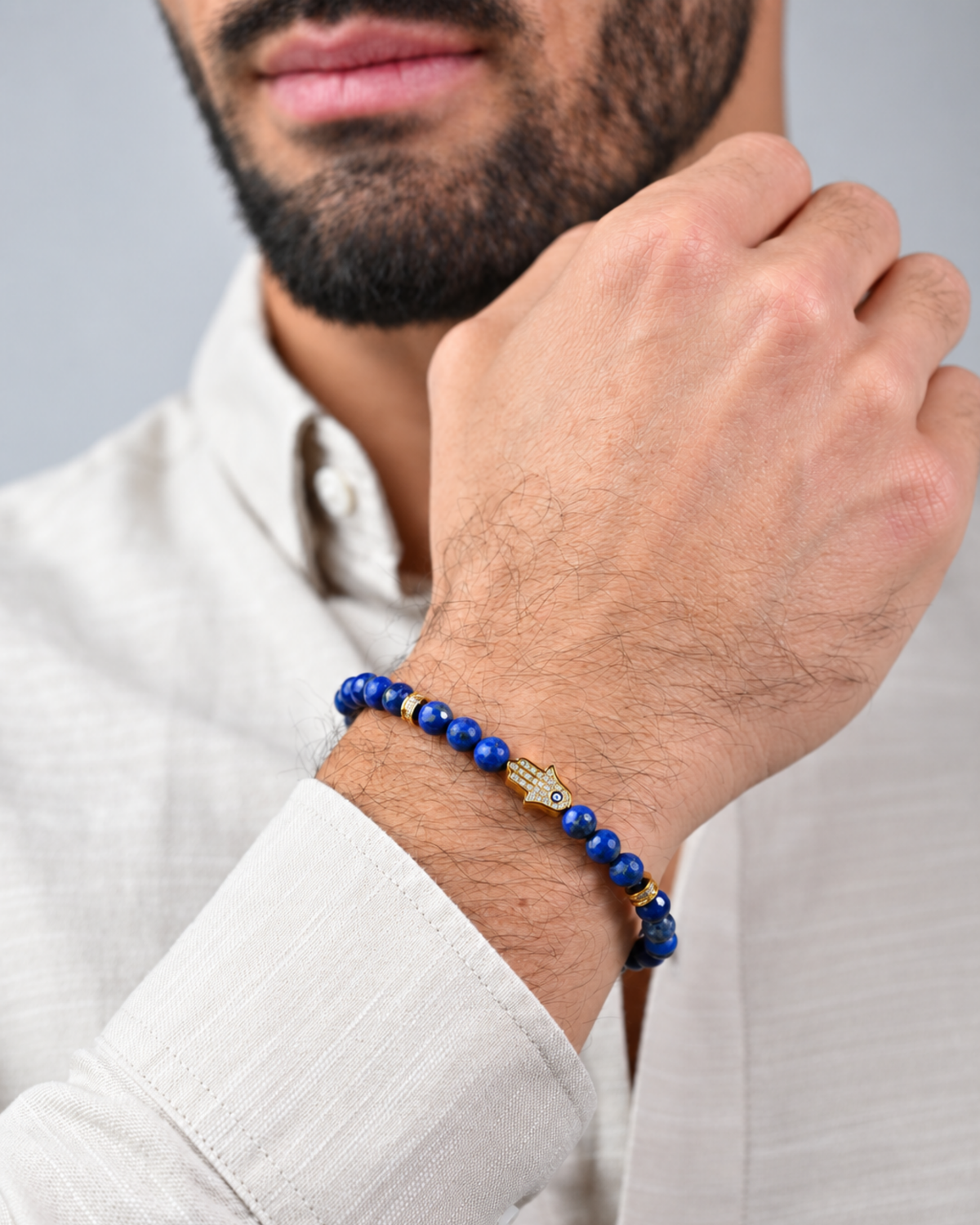 Lapis bead bracelet on wrist with gold charm and black cord, worn with white shirt.