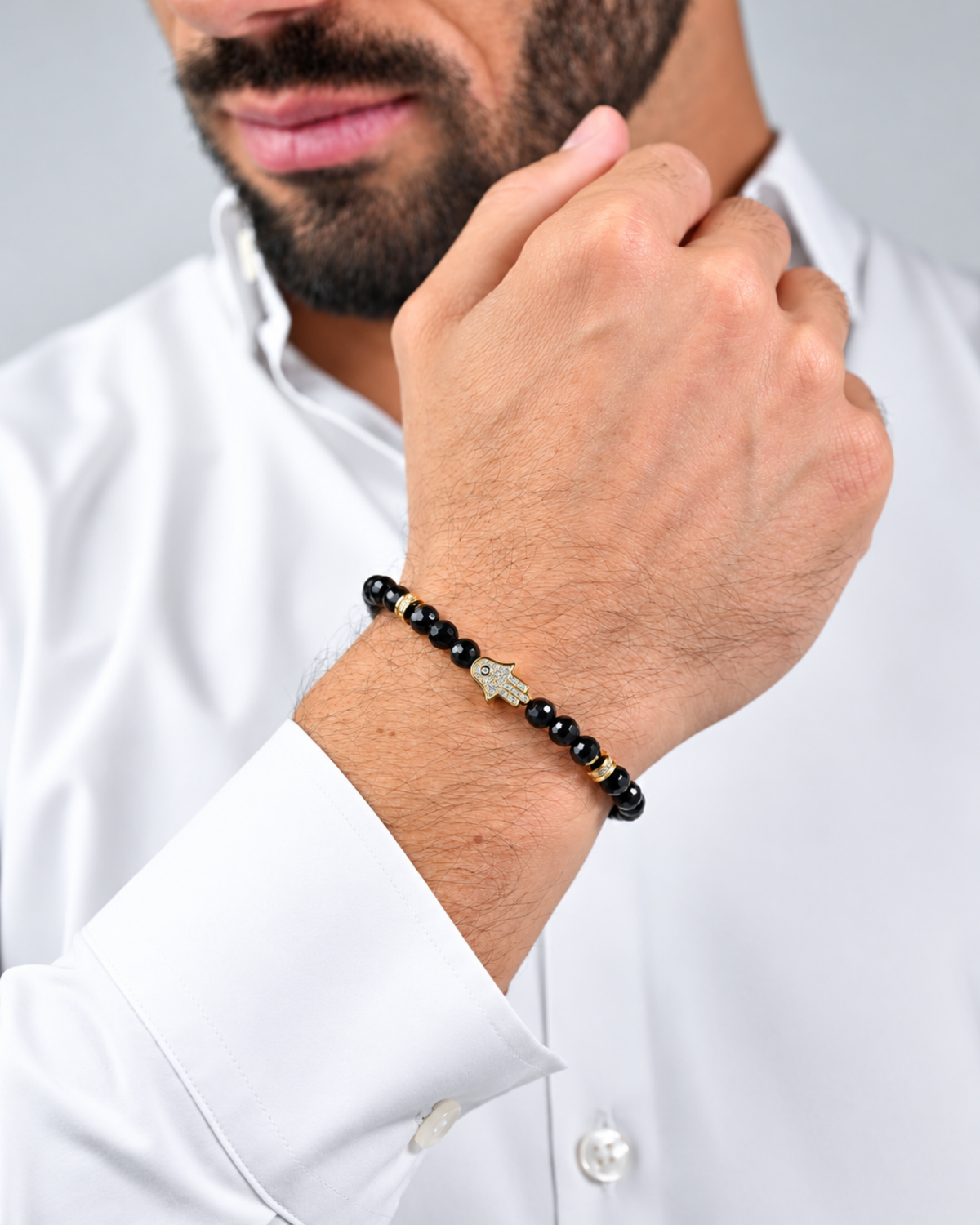 Black beaded bracelet with gold Hamsa charm on man’s wrist, adjustable cord.