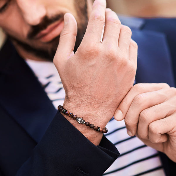 Tiger-eye bead bracelet on man's wrist with black cord and silver Hamsa charm
