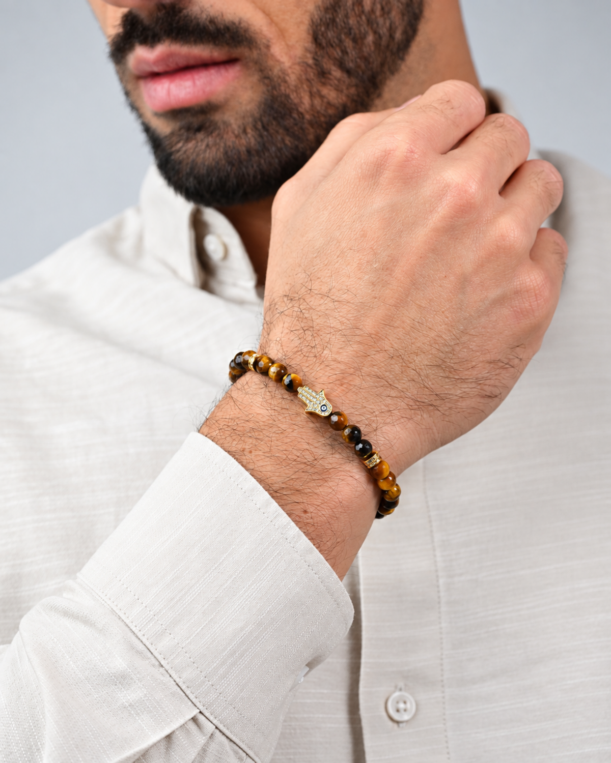 Tiger eye bead bracelet on wrist with gold hamsa charm and black beads, braided cord