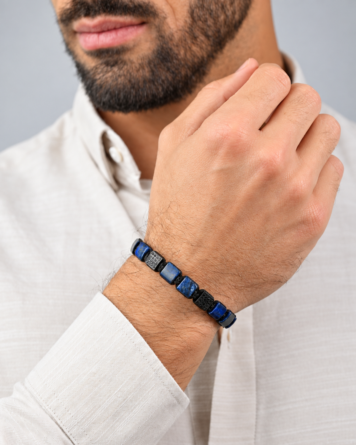 Blue and black bracelet on man's forearm, showing flat blue lapis-like beads and black cord
