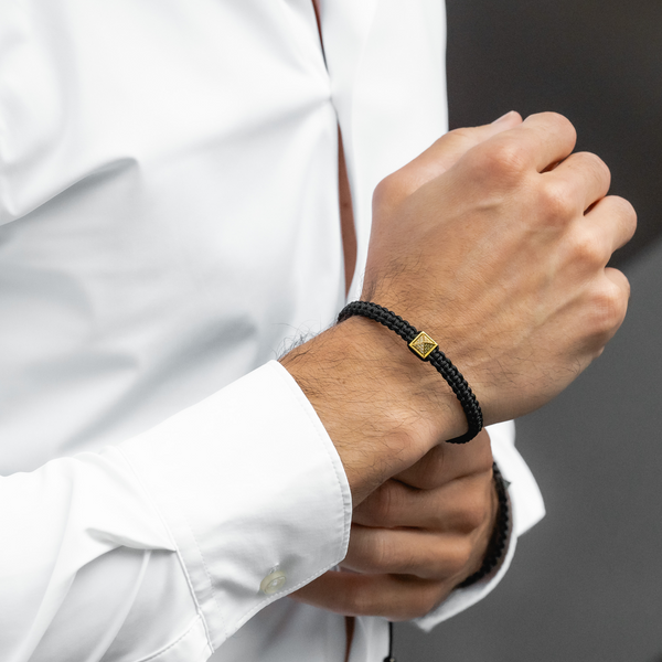 Black cord bracelet with gold pyramid charm worn on a man's wrist