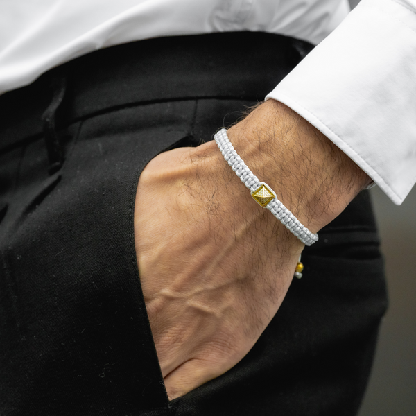 Men's pyramid bracelet on wrist: light gray cord with gold pyramid charm