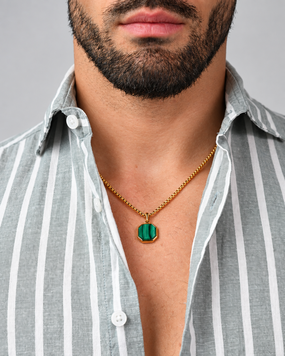 Gold chain necklace with green malachite octagonal pendant, worn with striped shirt