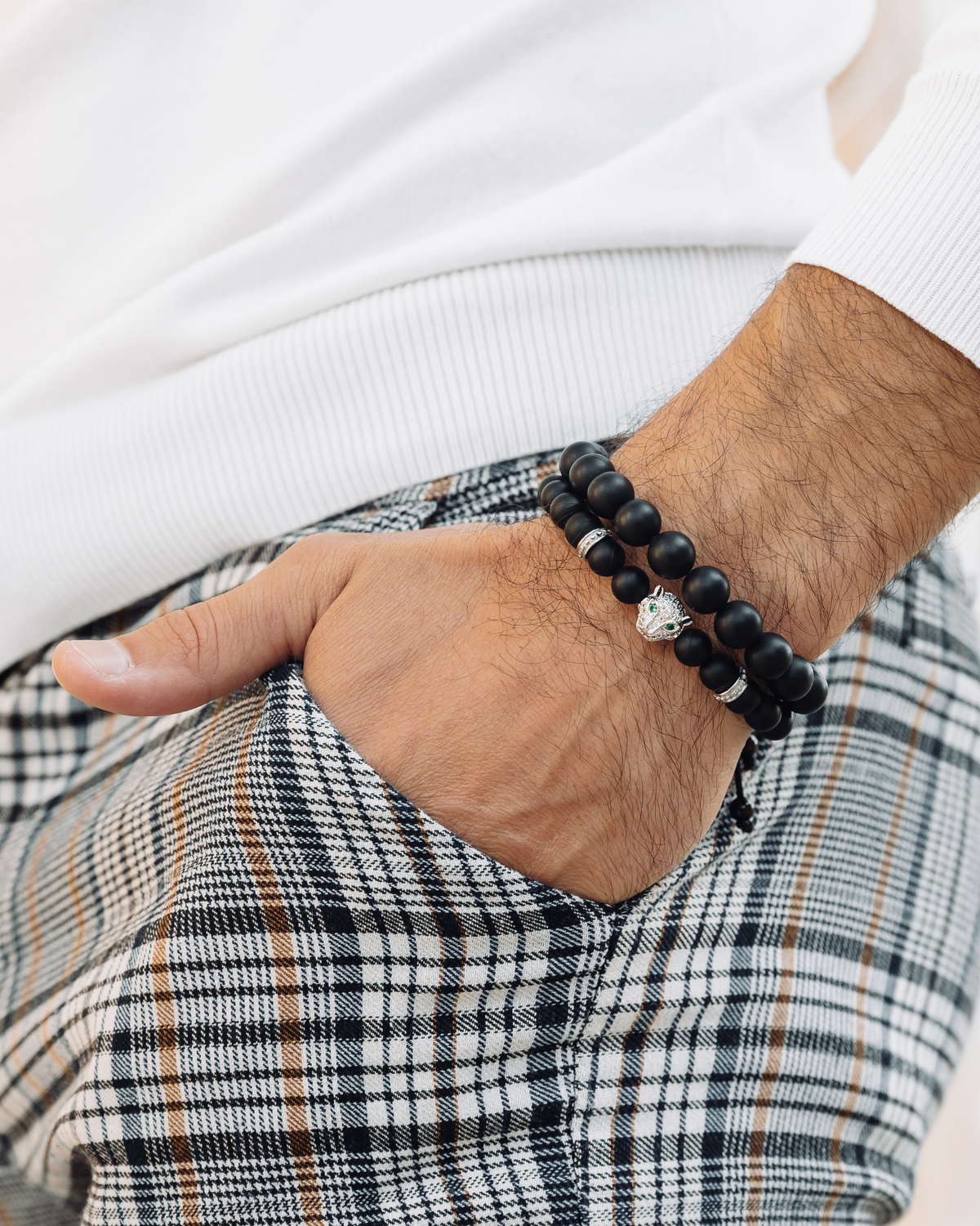 Black bead bracelet stack on wrist, with silver-tone charm bracelet and cord detail
