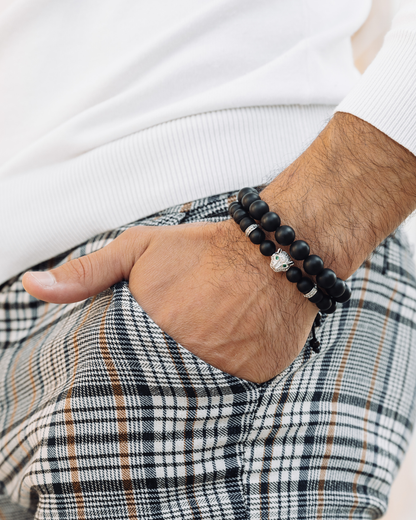 Black bead bracelet stack on wrist, with silver-tone charm bracelet and cord detail