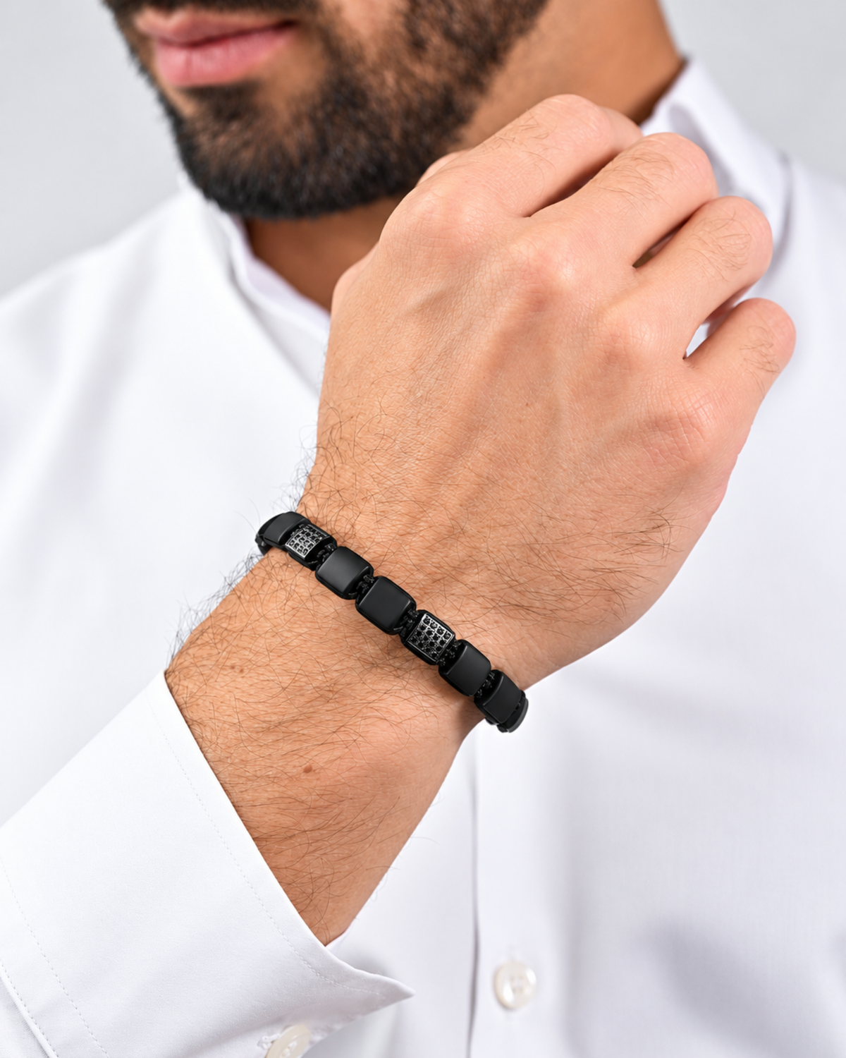 Black bead bracelet worn on wrist with braided cord and square black segments