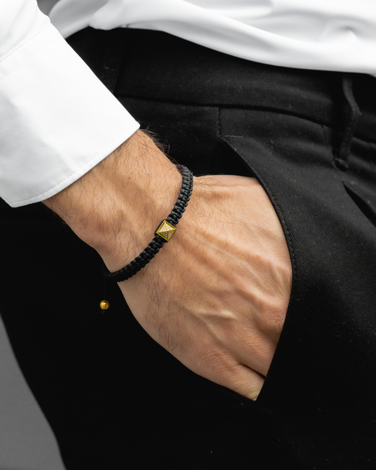 Black braided bracelet with gold pyramid zircon charm on wrist, adjustable beads